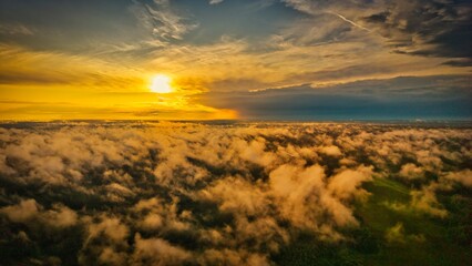A high-altitude aerial photograph capturing a sunrise above a vast forest with golden morning mist drifting through the treetops