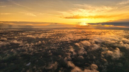 A high-altitude aerial photograph capturing a sunrise above a vast forest with golden morning mist drifting through the treetops