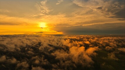 A high-altitude aerial photograph capturing a sunrise above a vast forest with golden morning mist drifting through the treetops