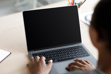 A teen afro American schoolgirl in glasses is focused on her laptop with an empty screen while studying at home. She is engaged in a video lesson, adapting to remote learning during quarantine.