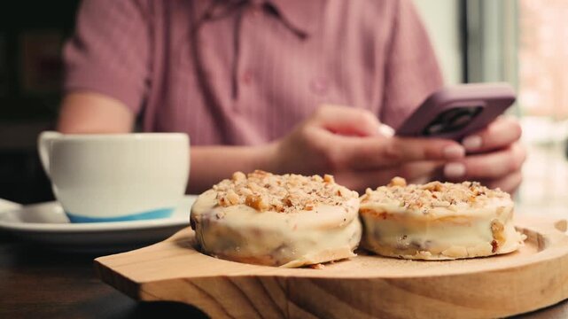 Woman sitting at cafe using phone, working, drinking coffee with traditional argentina dessert Alfajores. High quality 4k footage