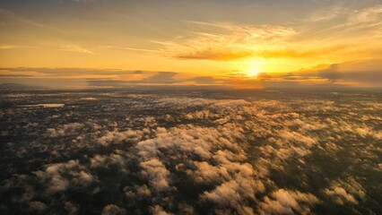 A high-altitude aerial photograph capturing a sunrise above a vast forest with golden morning mist drifting through the treetops