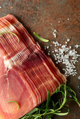 Sliced prosciutto and rosemary on a brown rusty background.
