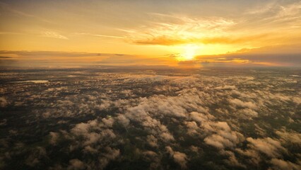 A high-altitude aerial photograph capturing a sunrise above a vast forest with golden morning mist drifting through the treetops