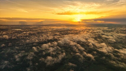 A high-altitude aerial photograph capturing a sunrise above a vast forest with golden morning mist drifting through the treetops