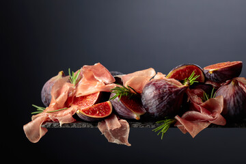 Prosciutto with rosemary and fig fruit on a black background.