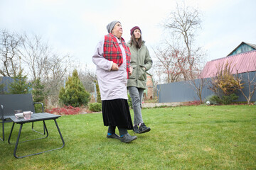 Warm winter walk: elderly woman and young adult strolling in garden
