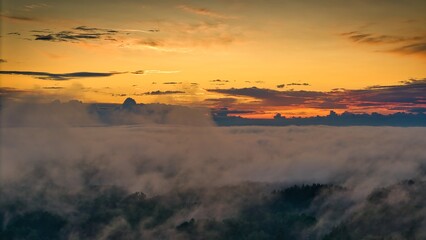 A high-altitude aerial photograph capturing a sunrise above a vast forest with golden morning mist drifting through the treetops