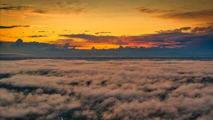 A high-altitude aerial photograph capturing a sunrise above a vast forest with golden morning mist drifting through the treetops