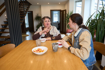 Two people engaged in conversation at home with coffee and snacks on wood table