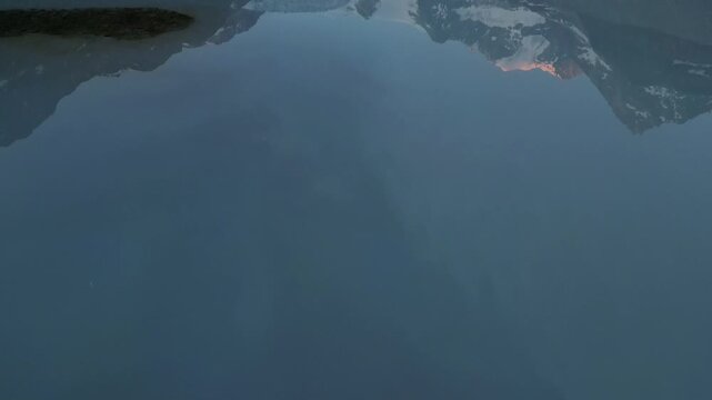 4K aerial drone shot of Glacier Moiry lake in Switzerland at sunrise, revealing turquoise water and snowy alpine peaks in the distance.