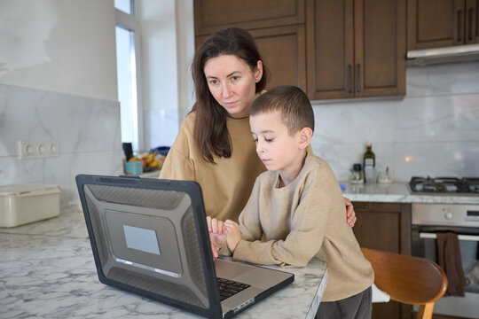 Mother and child using laptop in kitchen at home