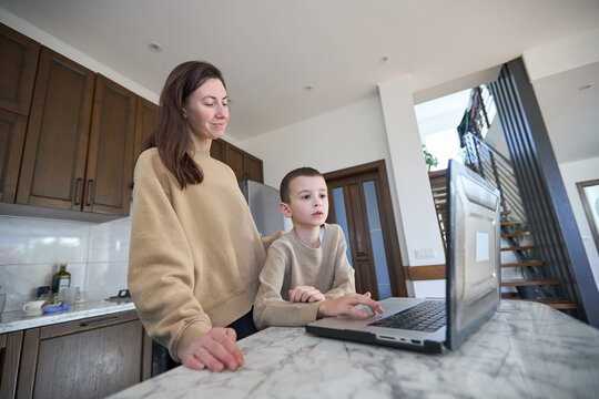 Mother and son learning at home using a laptop in a modern kitchen setting - Powered by Adobe