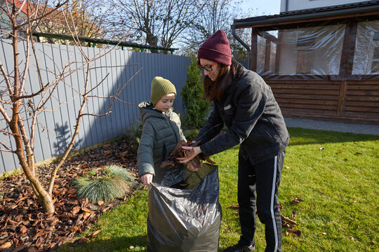 Mother and child collecting autumn leaves in sunny backyard - Powered by Adobe