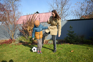 Mother and child play soccer in autumn garden