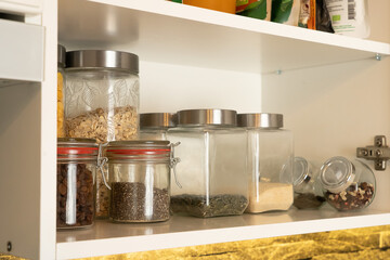 Organized pantry shelf with assorted grains, seeds and snacks in glass jars, creating a warm, practical kitchen look.