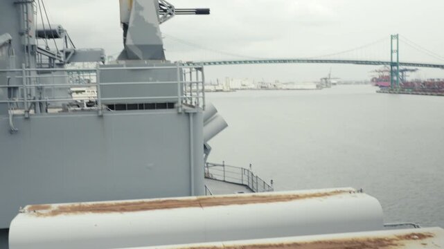 Upward panning shot from the lower deck of a US Navy destroyer revealing a radar-guided 20mm Vulcan cannon, with Los Angeles Harbour visible in the background. Clear daylight detail shot.