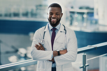 Portrait of handsome smiling young african american doctor in workwear and stethoscope with arms...