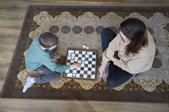 Top view of two people playing checkers on a patterned rug