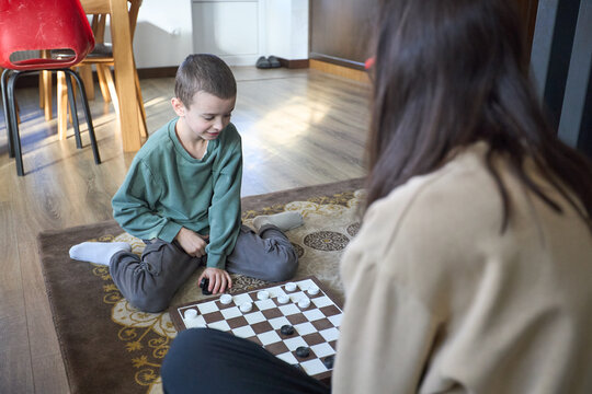 Mother and son playing checkers on carpet at home