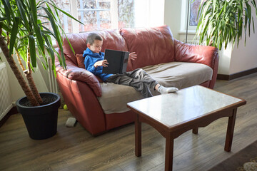 Child relaxing on couch playing with tablet in cozy living room setting