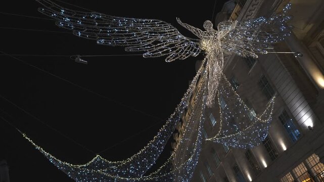 Illuminated angel light sculpture hanging over a London street at night.