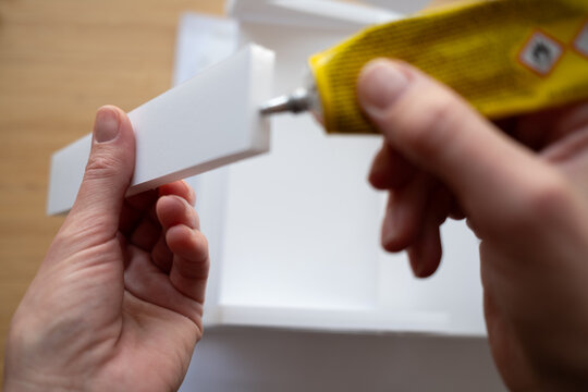 First-person view of hands applying glue to a white modeling block. A concept for DIY, crafting, and assembly projects. Selective focus on the creative process.