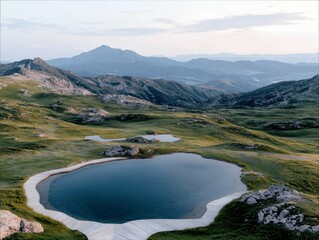 A serene landscape featuring a dark blue mountain lake with a curved wooden boardwalk, surrounded by rolling green hills and rocky outcrops. In the background,