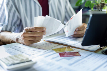 close up shot, asian man holding many receipt and financial bills from spending via credit card and calculate expenses before paying debt