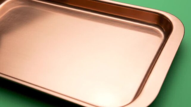 Close-up of a shiny copper tray on a green background.