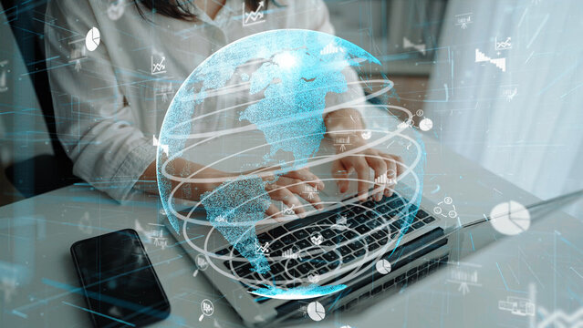 A woman engages with her laptop in a contemporary workspace, surrounded by a digital globe overlay, symbolizing advancements in technology and global connectivity. Xenic