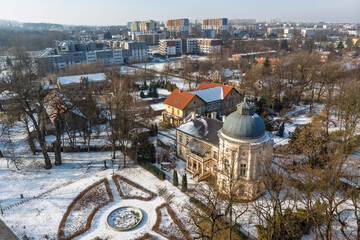Aerial view of the historic Jerzmanowski Manor (Pałac Jerzmanowskich) and surrounding park in Krakow, Poland, contrasted with modern residential estates in winter.