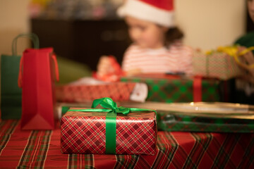 A festive scene with colorful wrapped box, holiday shopping bags, and a cozy plaid tablecloth, evoking the joy of Christmas gift-giving. In the background children are decorating gifts.