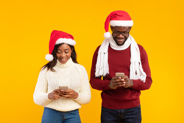Fototapeta premium A black couple is standing side by side, both wearing Santa hats and cozy sweaters.