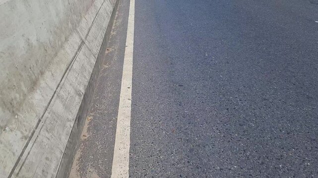 Asphalt road surface with concrete barrier and white line marking