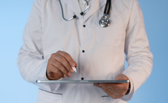 Doctor using digital tablet with stylus for medical data input on light blue background, showing modern healthcare technology concept..