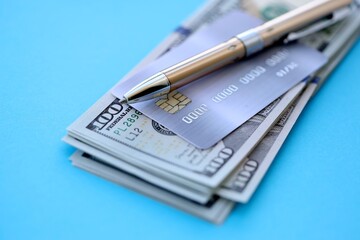 Credit card and pen with US dollar currency money bills banknotes on light blue background. Business, financial operations and accounting in United States of America