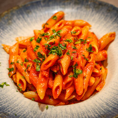 Delicious penne pasta served with rich tomato sauce and fresh parsley in a ceramic plate. Bright, appetizing food photograph ideal for menus, restaurants and advertising.
