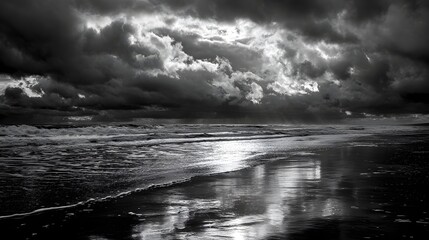 Dramatic black and white seascape with stormy clouds reflecting on the wet sand.