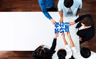 A diverse team works together to assemble a puzzle in an office setting, promoting collaboration and problem-solving. This top view captures the essence of teamwork and creativity. Amity