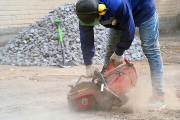 Construction worker cutting, Urban site stone cutting, Worker using power saw amid dust and sparks, Closeup of worker operating concrete saw with safety gear in motion