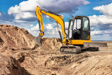 A yellow excavator is working hard to dig into a mound of sand on a construction site during a...
