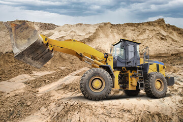 A large yellow loader is digging and moving dirt at an active construction site. The sky is...