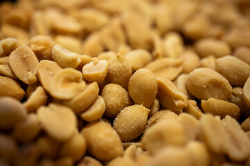 Macro texture of roasted salted peanuts heap. Close-up of shelled groundnuts background with salt. Delicious savory beer snack or healthy vegan food. Golden crunchy nut pile