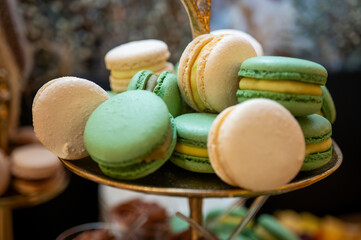 Close-up of beige vanilla macarons on a tray. Delicious French pastry dessert with cream and strawberry tarts in the blurred background. Sweet catering event concept, selective focus