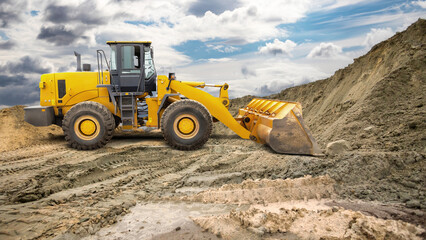 A yellow loader is seen digging and moving soil at a construction site under a dramatic sky filled with clouds on an overcast afternoon