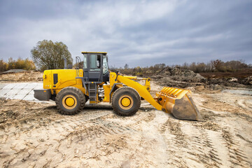 Obraz premium Construction equipment moves dirt at a site under a cloudy sky while preparing land for new development. Heavy machinery is actively engaged in work