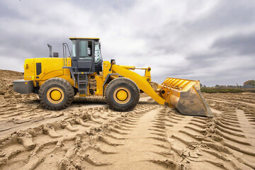 A large yellow loader operates at a construction site, moving dirt and shaping the ground under a...