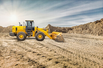 Obraz premium A yellow wheeled bulldozer or loader is working on a construction site, moving dirt and preparing the ground under a clear sky with bright sunlight