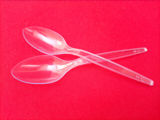 Disposable transparent plastic spoons on red background. Environmental Issue of plastic pollution concept